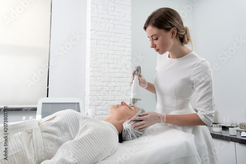 Bild auf Leinwand Mature woman receiving laser treatment in cosmetology clinic