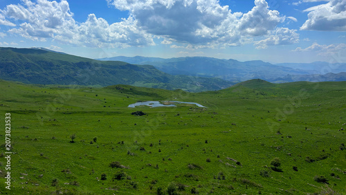 Panoramic Green Highland Valley with Mountains and Cloudy Sky