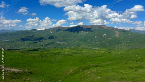 Panoramic Green Highland Valley with Mountains and Cloudy Sky