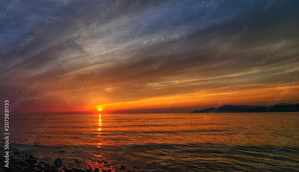 Naklejka premium Vivid orange sunset over the ocean with distant mountains on the horizon