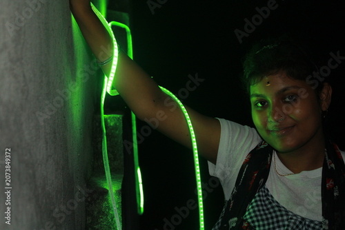 Creative portrait of a young Indian girl illuminated by vibrant green neon LED lights against a dark background. The dramatic lighting creates a futuristic atmosphere