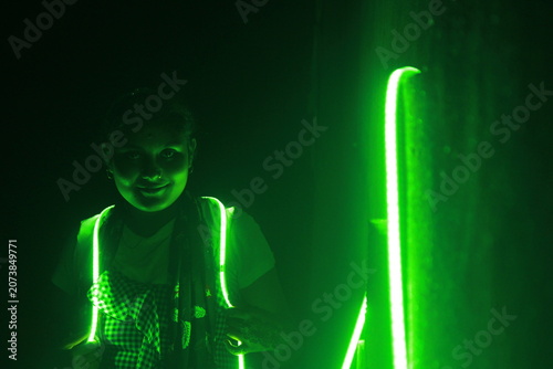 Creative portrait of a young Indian girl illuminated by vibrant green neon LED lights against a dark background. The dramatic lighting creates a futuristic atmosphere