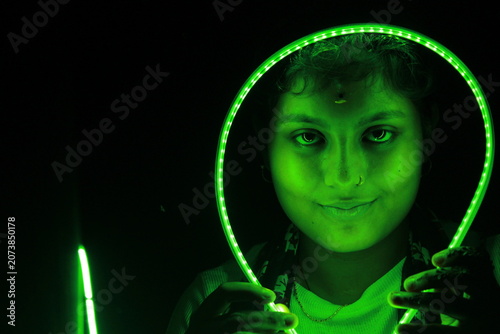 Creative portrait of young Indian woman framed by glowing green LED light against black background. Dramatic neon illumination creates futuristic and artistic atmosphere