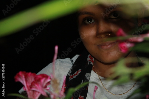 Portrait of a young Indian woman posing beside flowering plants in an outdoor garden at night. The image captures natural beauty, confidence, and contemporary Indian lifestyle, with vibrant flowers