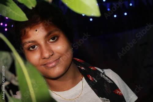 Portrait of a young Indian woman posing beside flowering plants in an outdoor garden at night. The image captures natural beauty, confidence, and contemporary Indian lifestyle, with vibrant flowers