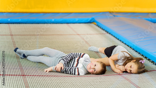 Fotografija Happy smiling small kids laying on indoor trampoline in entertainment center hav