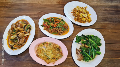 Traditional Thai family style meal with assorted savory dishes served on a rustic wooden dining table.