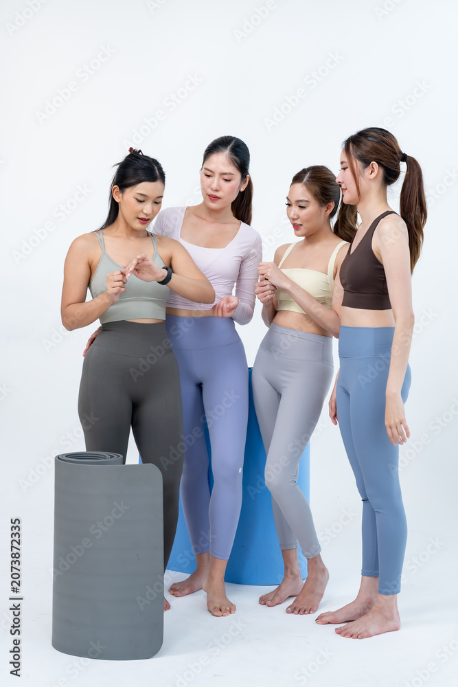 Obraz premium Asian women friends stand together beside rolled yoga mats, discussing wellness plan in minimal studio, trainer shares guidance for flexibility goals, posture balance, healthy fitness routine