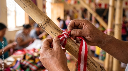 Skilled hands tying red and white ribbon onto bamboo pole for decoration.