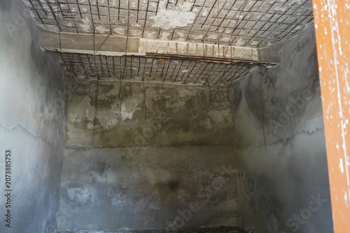 Interior of a dark, abandoned concrete room with severely stained walls and dangerously exposed, rusting iron rebar hanging from the deteriorating ceiling.