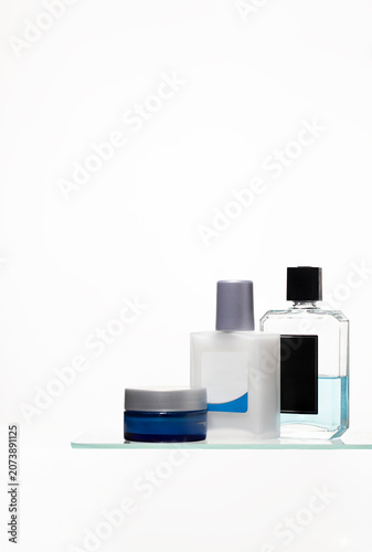 Canvastavla Modern men's skincare set featuring a deep blue face cream jar, white aftershave balm, and clear glass cologne bottle on a minimalist glass shelf