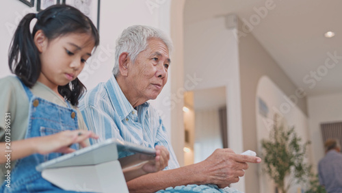 Obraz na plátně Asian grandfather and granddaughter spending time together at home, sharing learning, family love, care, and meaningful intergenerational moments