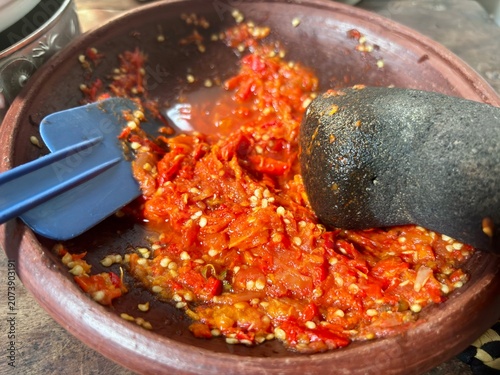 Photos Traditional Indonesian chili sambal being prepared in a clay mortar with a stone pestle