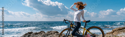 Solo Journey by the Sea: A lone woman with a bicycle stands on a rocky coastline, gazing out at the vast blue ocean under a cloudy sky, embracing the freedom of exploration and the beauty of nature.