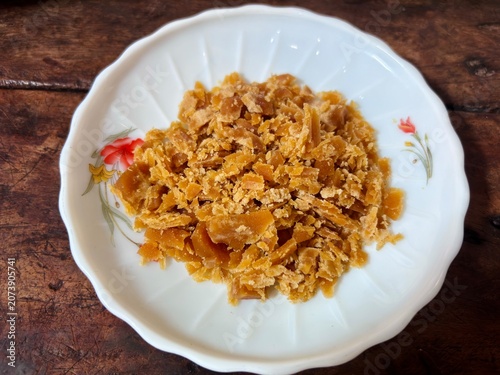 Photos Top view of chopped or grated Indonesian palm sugar or gula jawa served on a white floral ceramic plate over a rustic wooden table background, fresh sweet cooking ingredient and sweetener