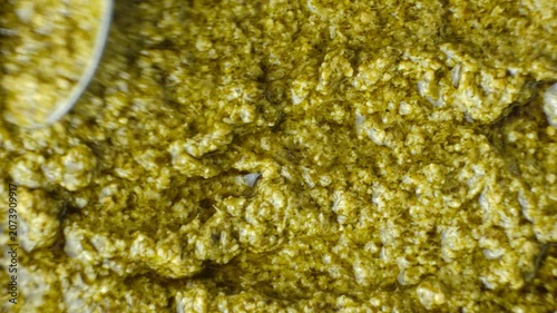 Top view of a spoon sliding over green basil pesto smoothing the surface