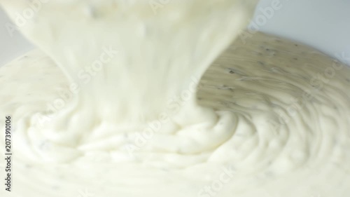 Creamy tartar sauce pouring into a bowl close up