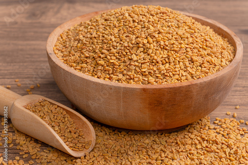 Bild auf Leinwand Heap of raw fenugreek seeds in wooden bowl with wooden scoop on rustic wooden su