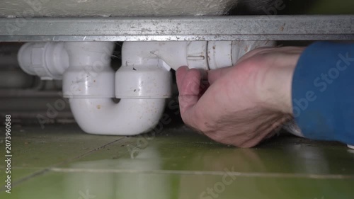 Plumber repairing a plastic siphon under the bathtub close-up, Close-up of hands repairing a leaking drain pipe under the bath