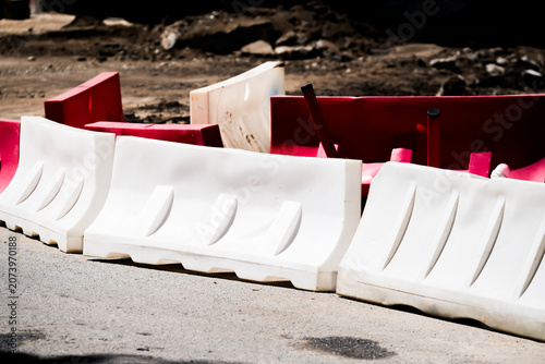 Series of red and white road barriers placed along an active urban construction area during infrastructure maintenance works
