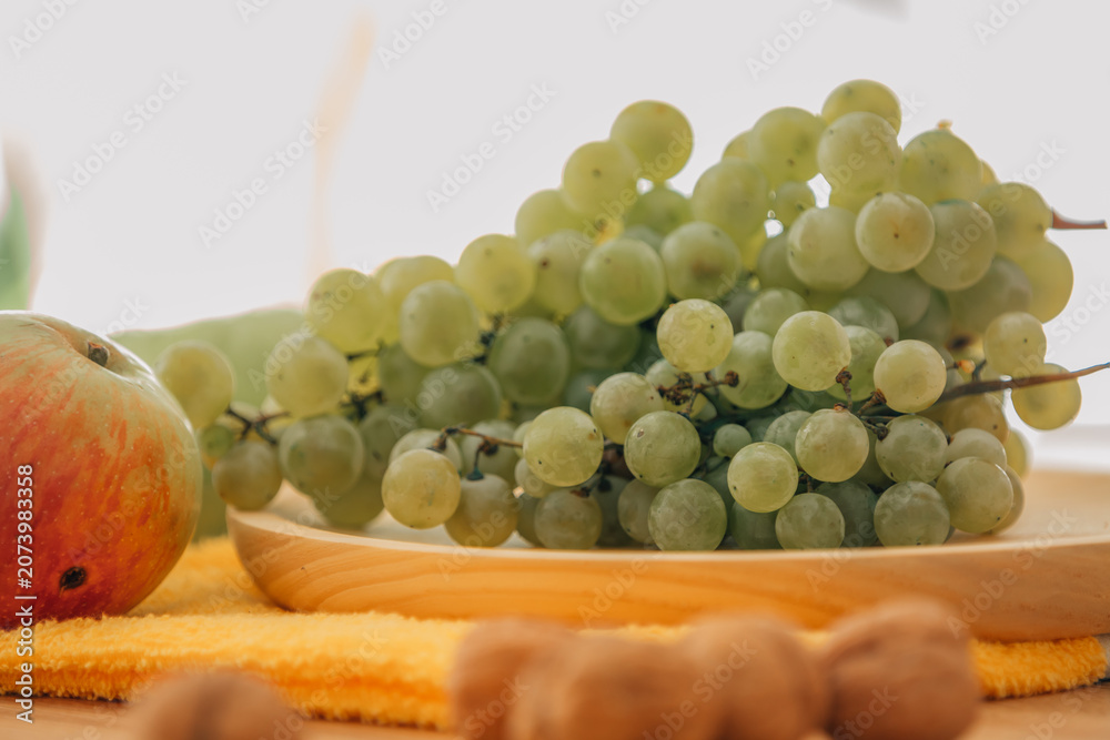Fototapeta premium Fresh green grapes, red and green apples, and walnuts arranged on a wooden tray — perfect for healthy eating, nutrition, and organic lifestyle concepts