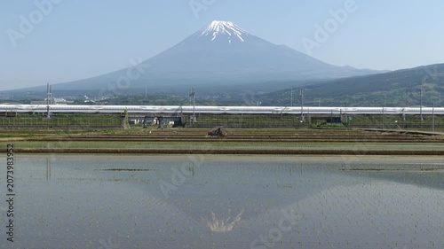 Mount Fuji reflected in serene rice paddies with a tractor cultivating fields and a Shinkansen railway in a beautiful Japanese spring landscape in Fuji City, Shizuoka (Real Time | Static | No Audio)