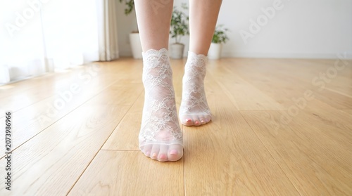 Front view of female feet walking forward in white lace ankle socks on wooden floor cozy lifestyle concept
