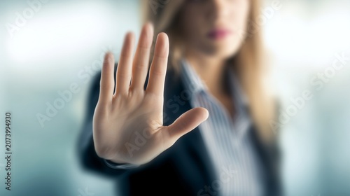 Professional business woman, businesswoman wearing a dark blazer extends her hand forward in a clear gesture to stop or block unwanted actions while working inside an office, showing rejection
