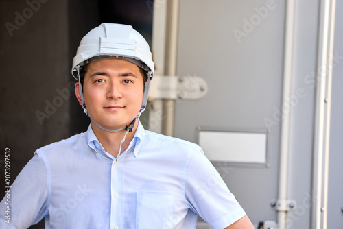 Photos 配達用のトラックの荷台の前でヘルメットを被ったカメラ目線で笑顔の物流の仕事をする運送業の男性
