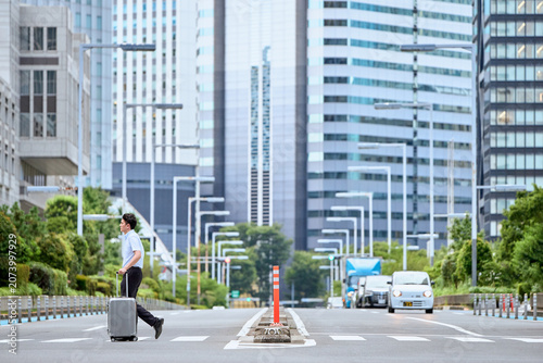 Tableau sur toile 都会のビジネス街の横断歩道をキャリーケースを持って歩く仕事で出張中の30代の日本人のビジネスマンの男