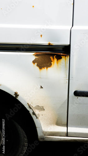 White utility vehicle showing rust corrosion, paint damage and structural wear on exterior body panel indicating long-term exposure and neglect