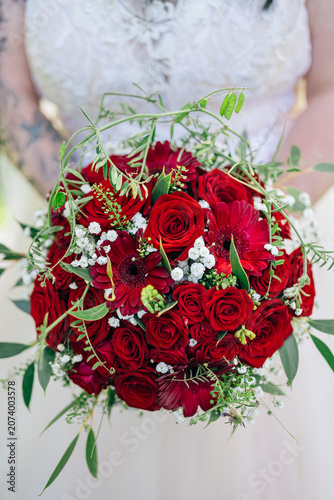 Fotografie Braut hält einen eleganten, runden Hochzeitsstrauß aus roten Rosen und Gerbera v