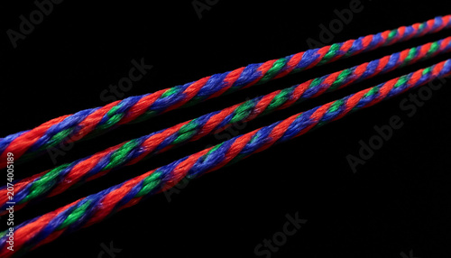 Three ultra-thin strand composed of vibrant red, blue, and green fibres, isolated against a deep black background. Shot in extreme perspective