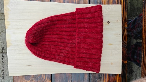 Red ribbed knitted beanie hat on a light wooden board. Handmade winter wool cap on a rustic wooden background