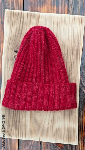 Vertical close up of a red ribbed knitted beanie hat on a light wooden board. Handmade winter wool cap on a rustic tabletop