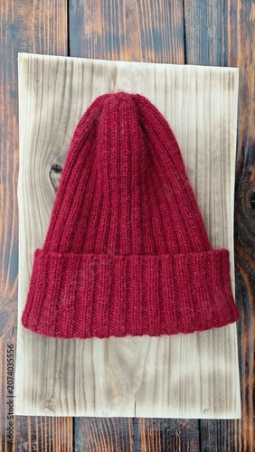 Red ribbed knit beanie hat on a light wooden board. Handmade winter cap on rustic background. Vertical photo