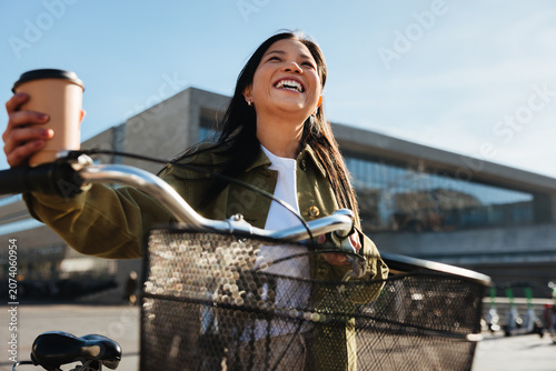 Woman with bicycle holding coffee, smiling on commute