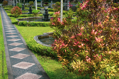 Patterned stone pathway through manicured gardens with ponds and shrubs at Tirta Gangga water palace, Karangasem, East Bali, Indonesia.