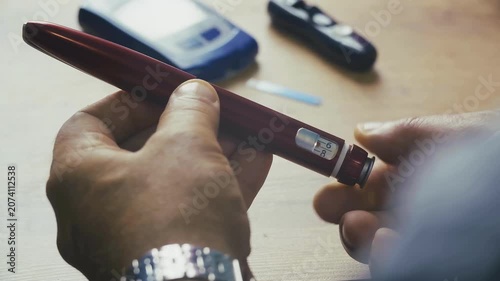 the hands of a man holding a burgundy insulin pen.