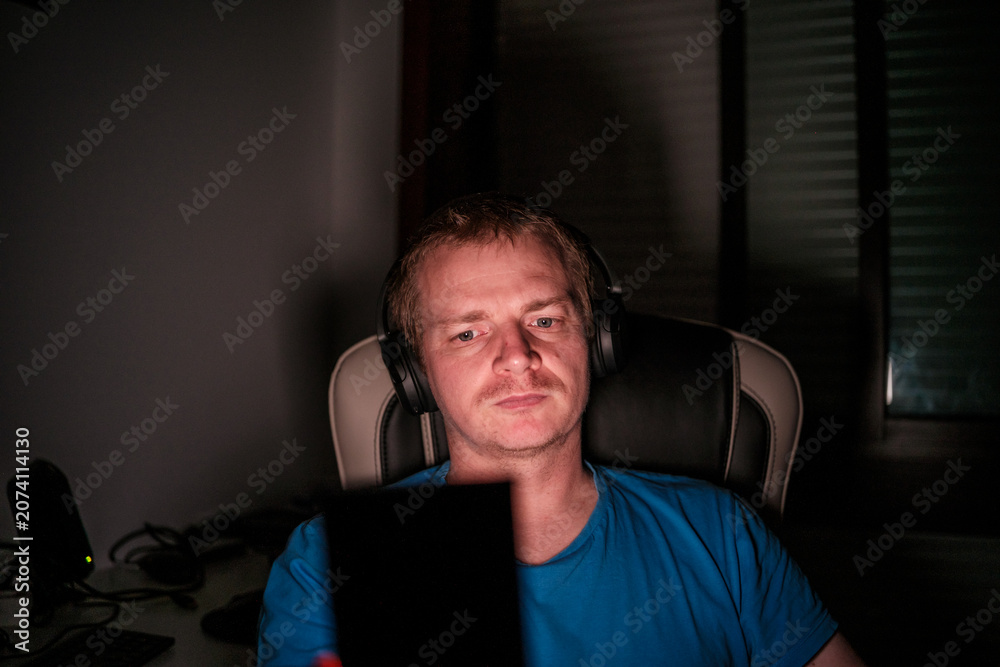 Fototapeta premium Man wearing headphones playing video games at night