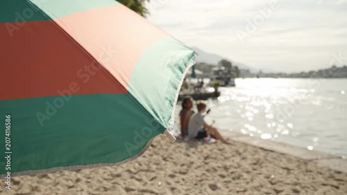 Relaxing Day at the Beach Under a Colorful Umbrella with Friends Enjoying the Sunshine by the Water's Edge Amidst Golden Sands and Gentle Waves