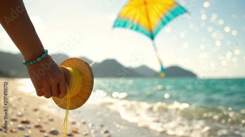 A Hand Gripping a Spool of String on the Beach as a Colorful Kite Flies Over the Sparkling Sea in the Distance Showcasing a Vibrant Summer Scene