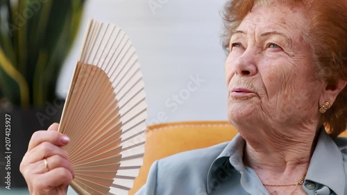 elderly woman fans herself during the summer heat wave, dealing with the extreme heat, highlighting the importance of caring for the elderly and raising awareness about the health 