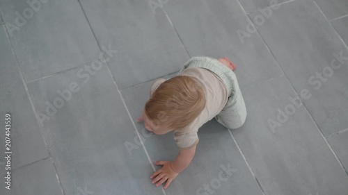 Child exploring indoors. Young child investigating and moving across modern indoor flooring happily. Baby with bright blond hair advances on smooth ceramic tiles