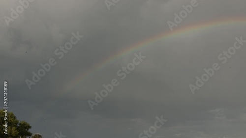 Vibrant rainbow arcs across a dramatic, cloudy sky after a storm