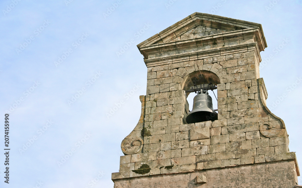 Fototapeta premium Old Stone Bell Tower. A historic European church steeple stands against a clear blue sky in the Languedoc region of South East France.