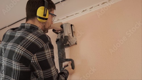 Electrician in protective gear uses wall chaser tool for cutting channels during electrical wiring installation work