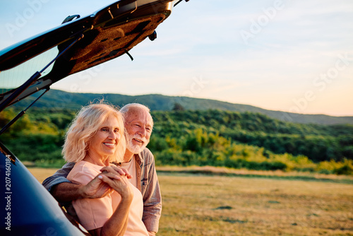 Foto Happy mature couple embracing beside their car, smiling and looking at the sunse