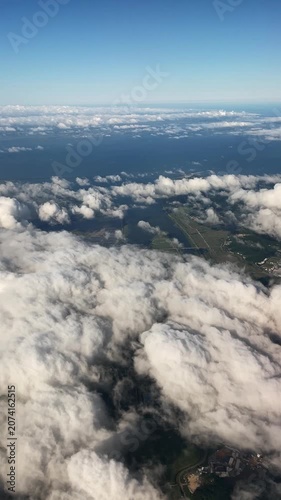 Aerial cloud progression over coastal farmland with dense cumulus shifting into thin band under clear blue sky during airplane descent and forward motion above fields, roads