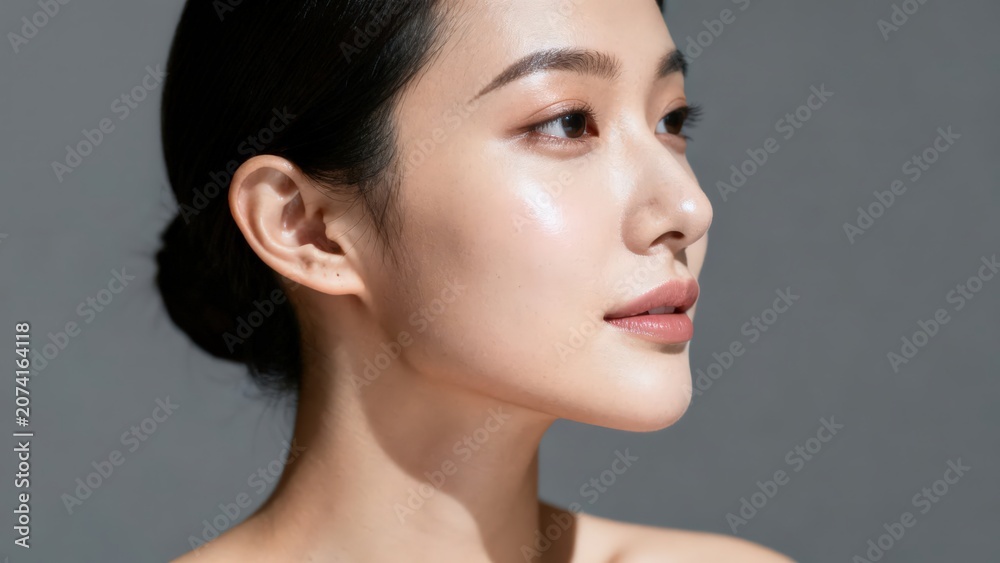 Fototapeta premium Serene asian woman with glowing skin posing in profile for a studio portrait on grey background.